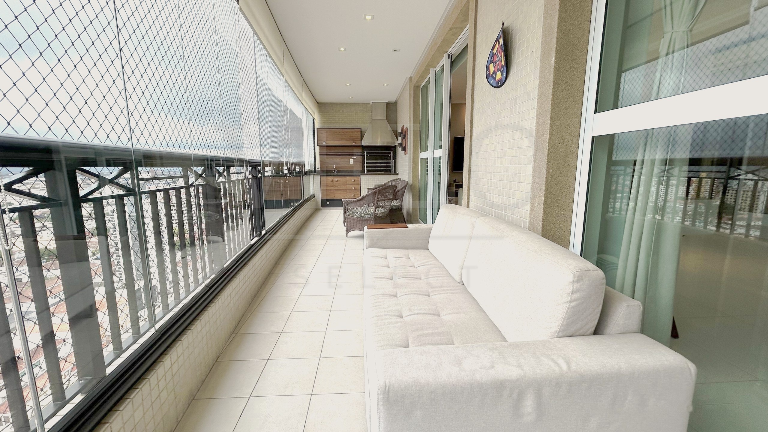 Varanda ampla e arejada de apartamento em Santos, com sofá claro e área gourmet